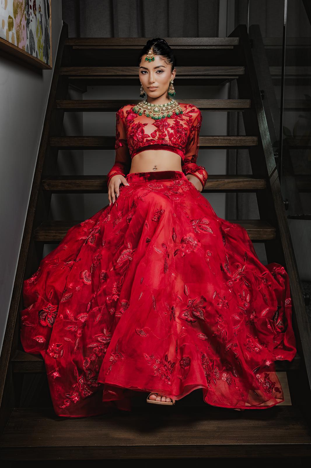 Bride in stunning red lehenga with emerald kundan jewellery set on staircase